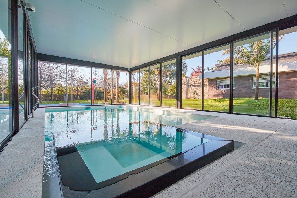 Lujosa piscina interior con amplios ventanales y vistas al jardín en Uruguay, fotografiada por RUMA Estudio.